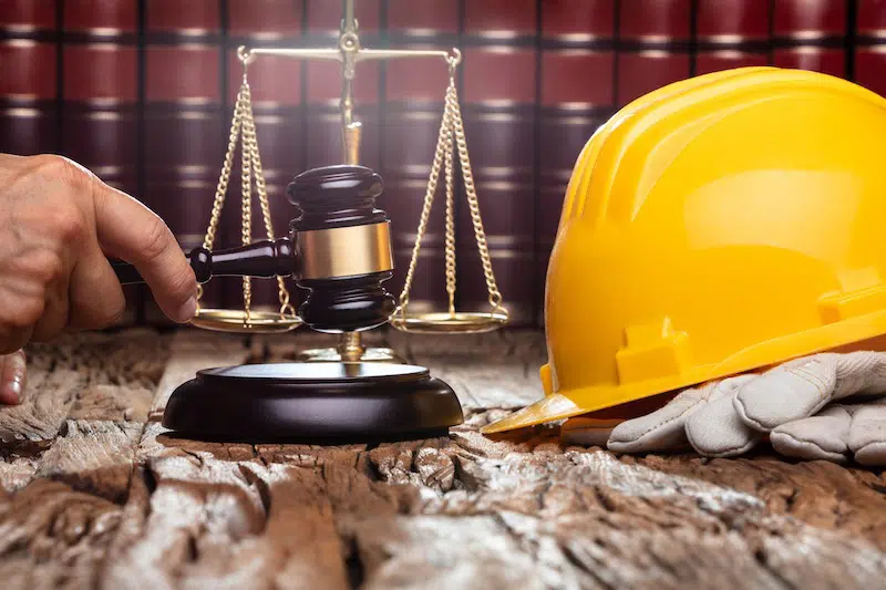 Judge Striking Gavel In Front Of Yellow Safety Helmet On The Wooden Table